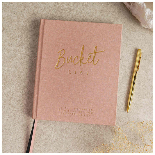 Pink notebook titled 'Bucket List' with a gold pen on a textured surface